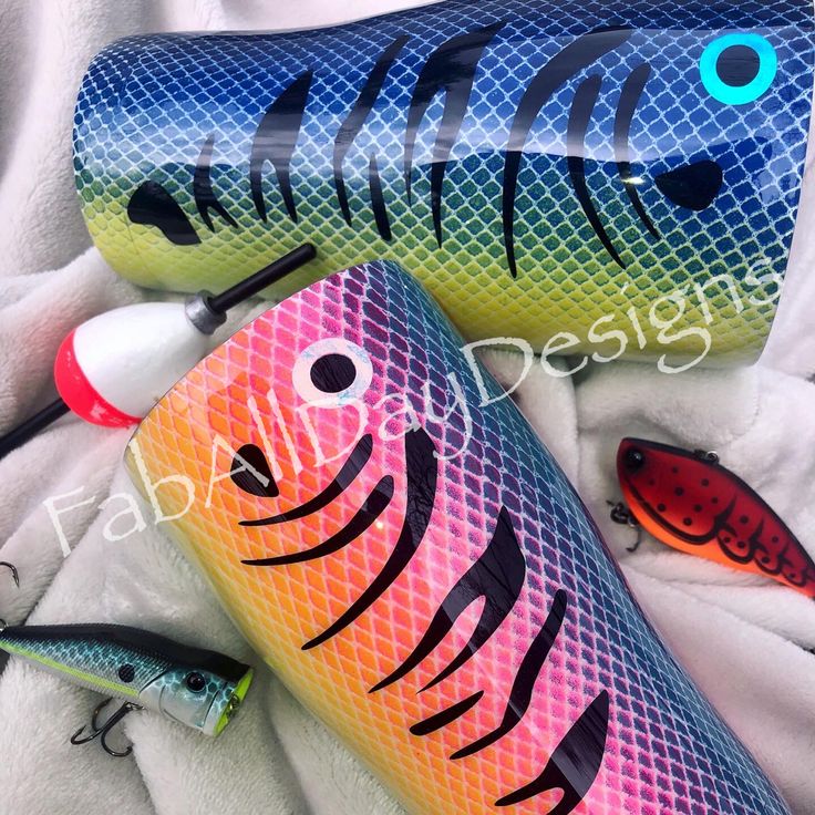 two colorful fish shaped water bottles sitting on top of a white blanket next to fishing lures