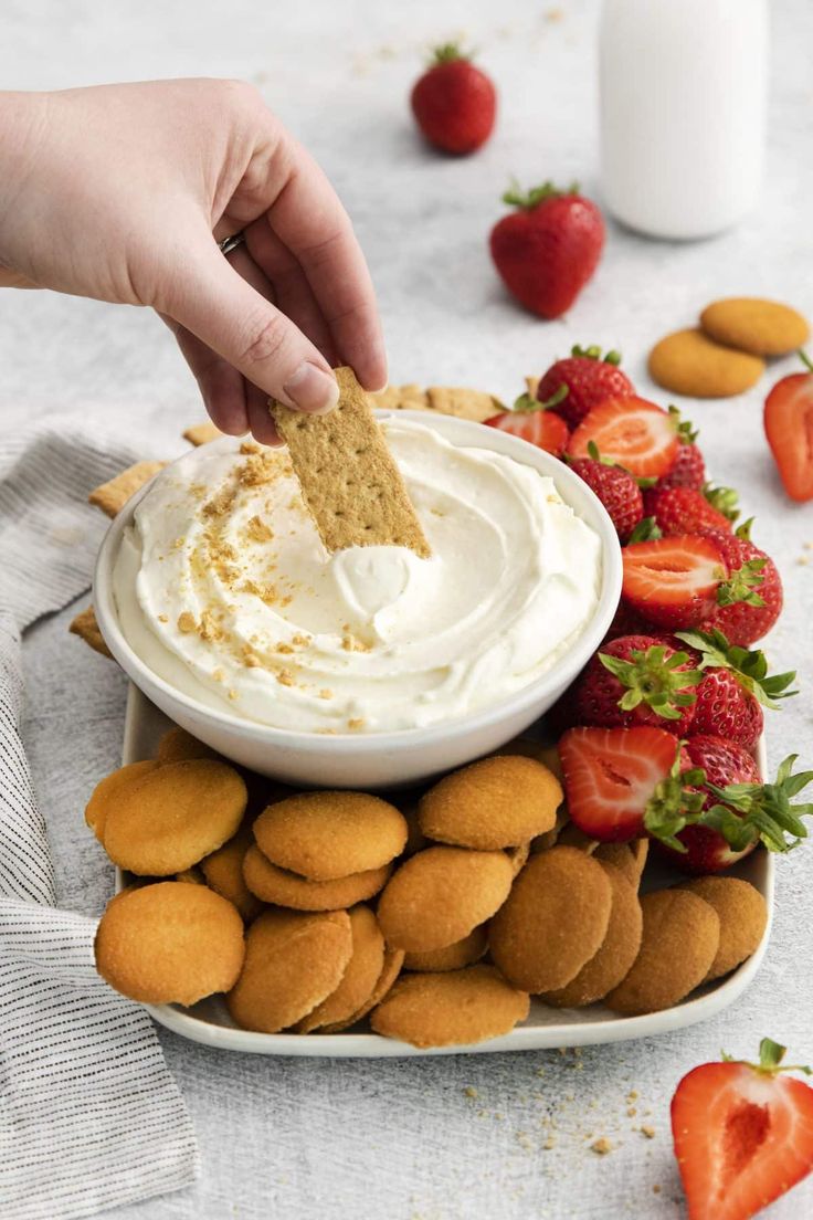 someone dipping some food into a bowl with strawberries and almonds on the side