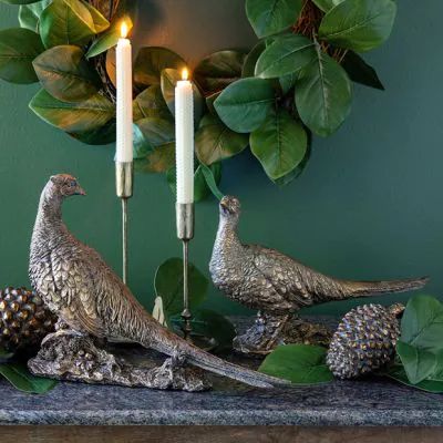 two pheasants on a table with pine cones and candles