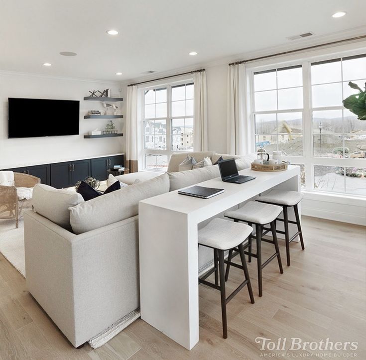 a living room filled with white furniture and lots of windows next to a kitchen area