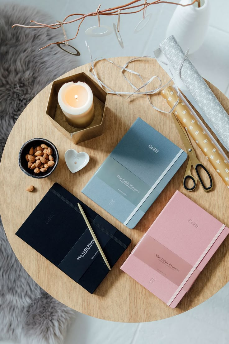 a wooden table topped with notebooks next to a bowl of nuts and a candle