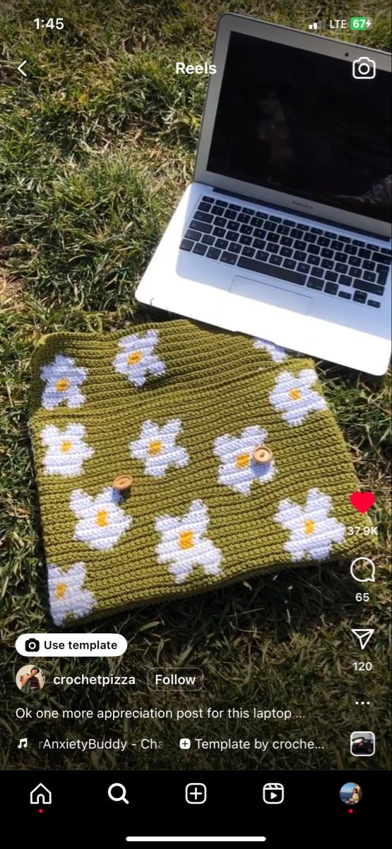 an open laptop computer sitting on top of a grass covered field next to a flowery blanket