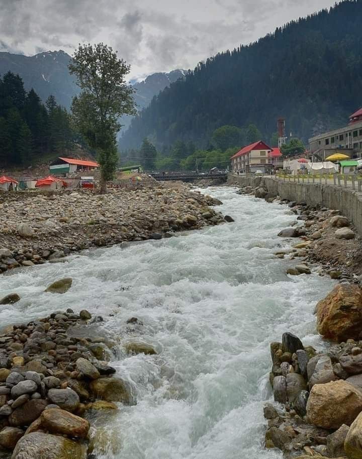 a river running through a lush green forest filled with rocks and water surrounded by mountains