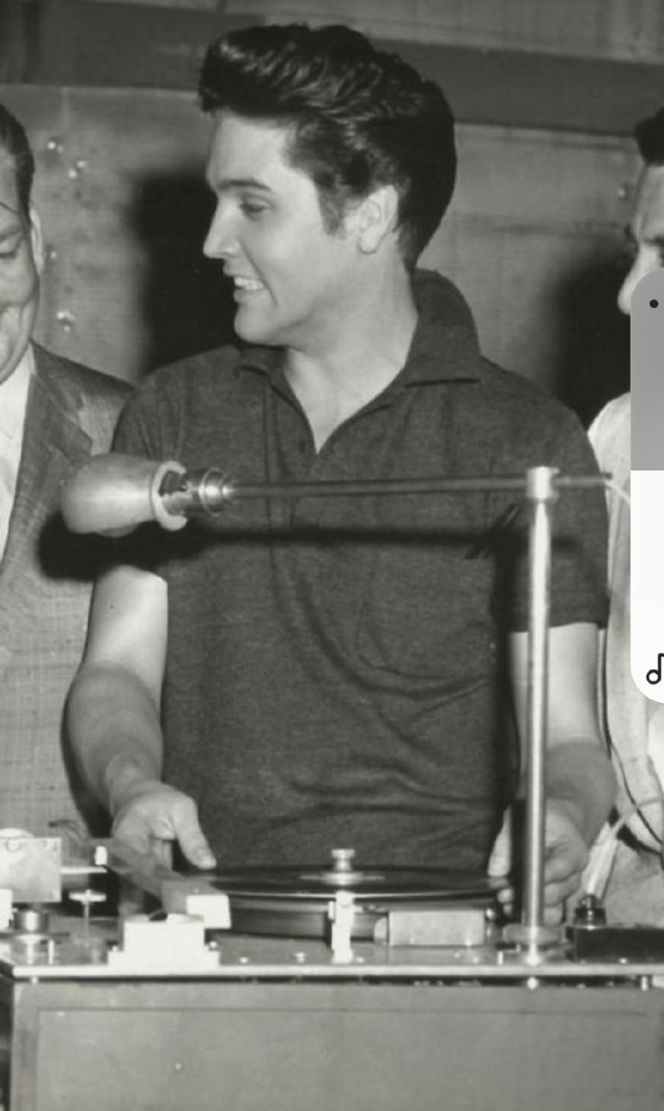 three men standing next to each other in front of a record player