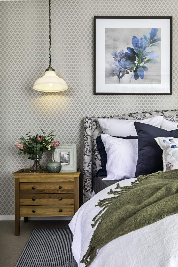 a bed sitting next to a dresser with flowers on top of it and a painting above it