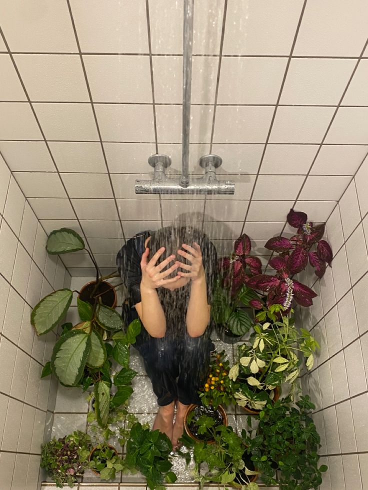 a person is sitting in the shower with plants