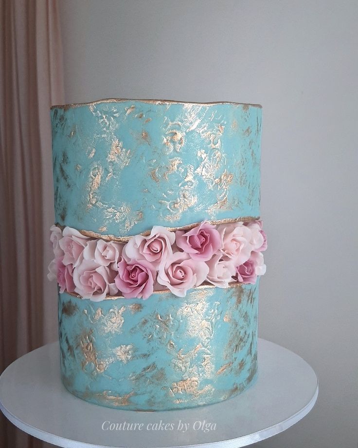 a blue and gold cake with pink flowers on top is sitting on a white table