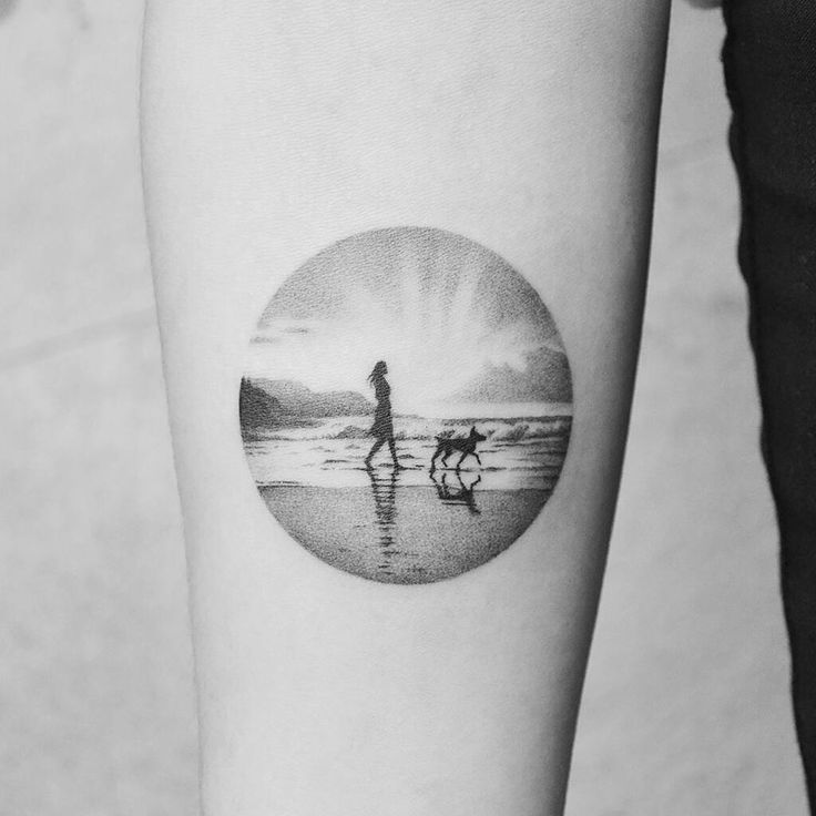 a person with a dog walking on the beach in front of an ocean sunset tattoo