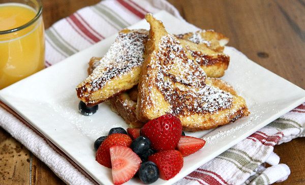 french toast with powdered sugar and berries on a plate next to a glass of orange juice