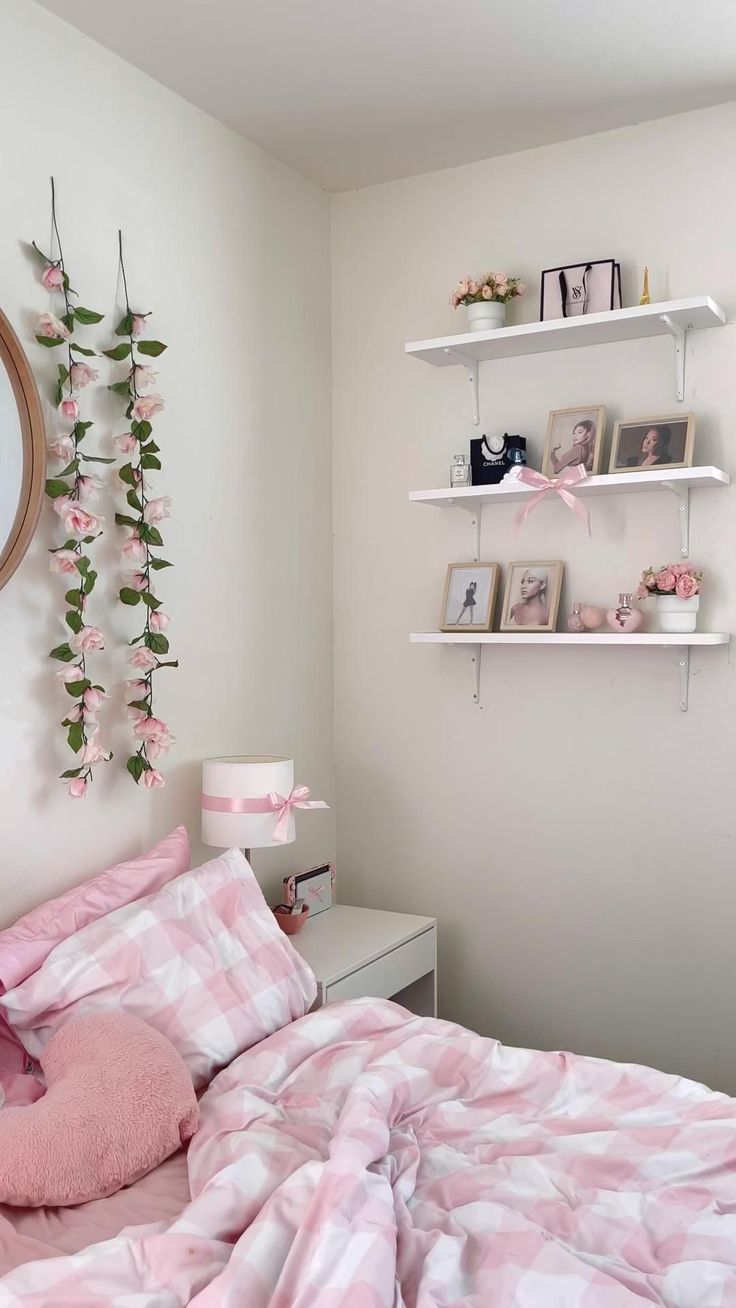 a bedroom with pink and white bedding, shelves and flowers on the wall above it