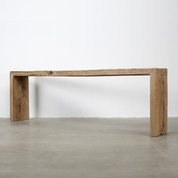 a large wooden bench sitting on top of a cement floor next to a white wall