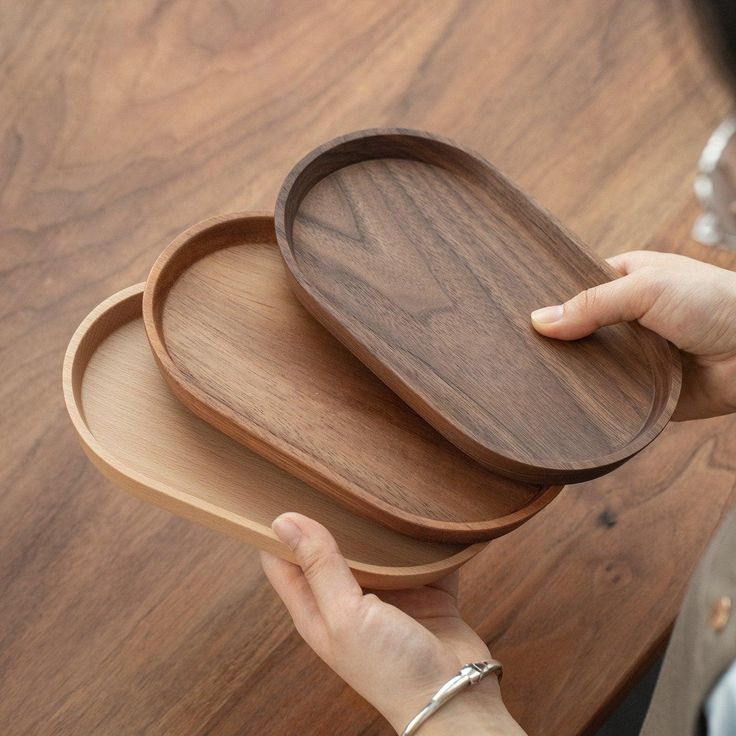 a person holding two wooden trays on top of a wooden table next to each other