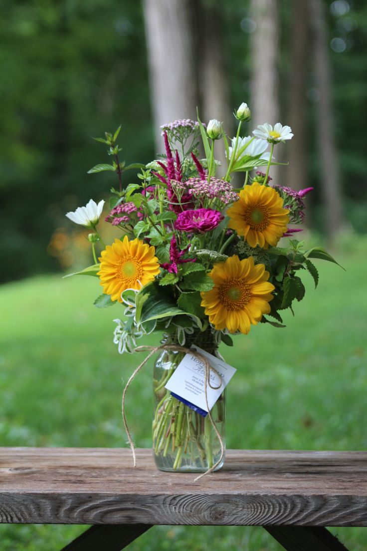 a bouquet of wildflowers and daisies in a mason jar on a picnic table