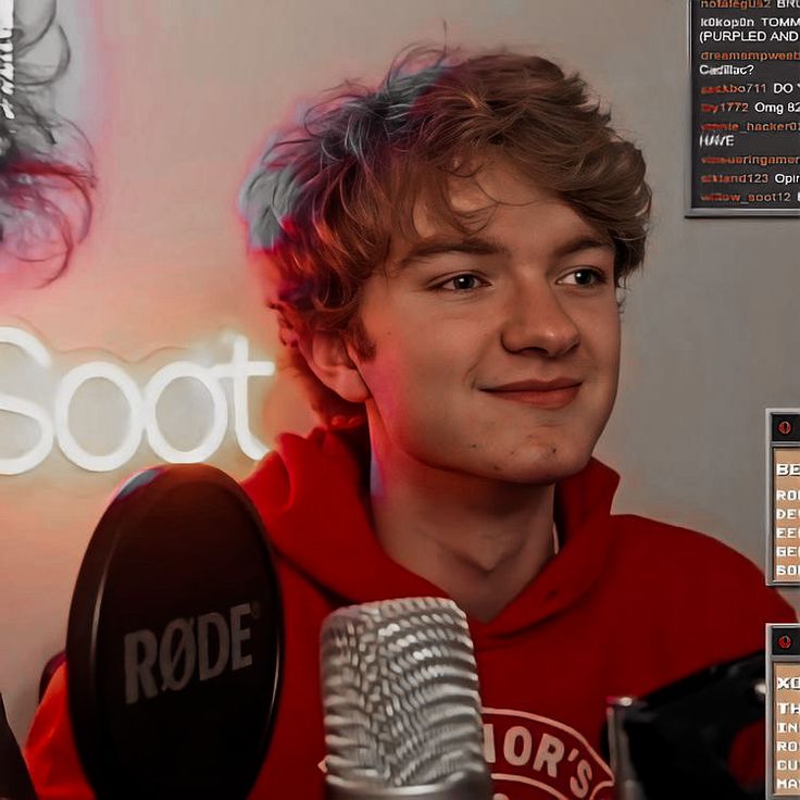 a young man holding a microphone in front of a neon sign that reads soot