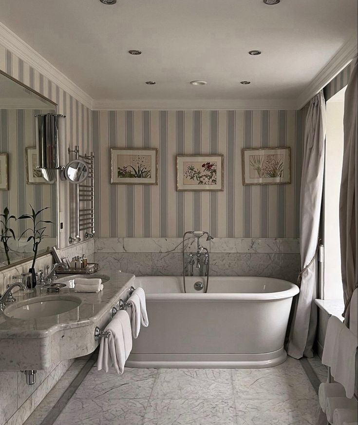 an elegant bathroom with striped walls and marble counter tops, along with two white bathtubs