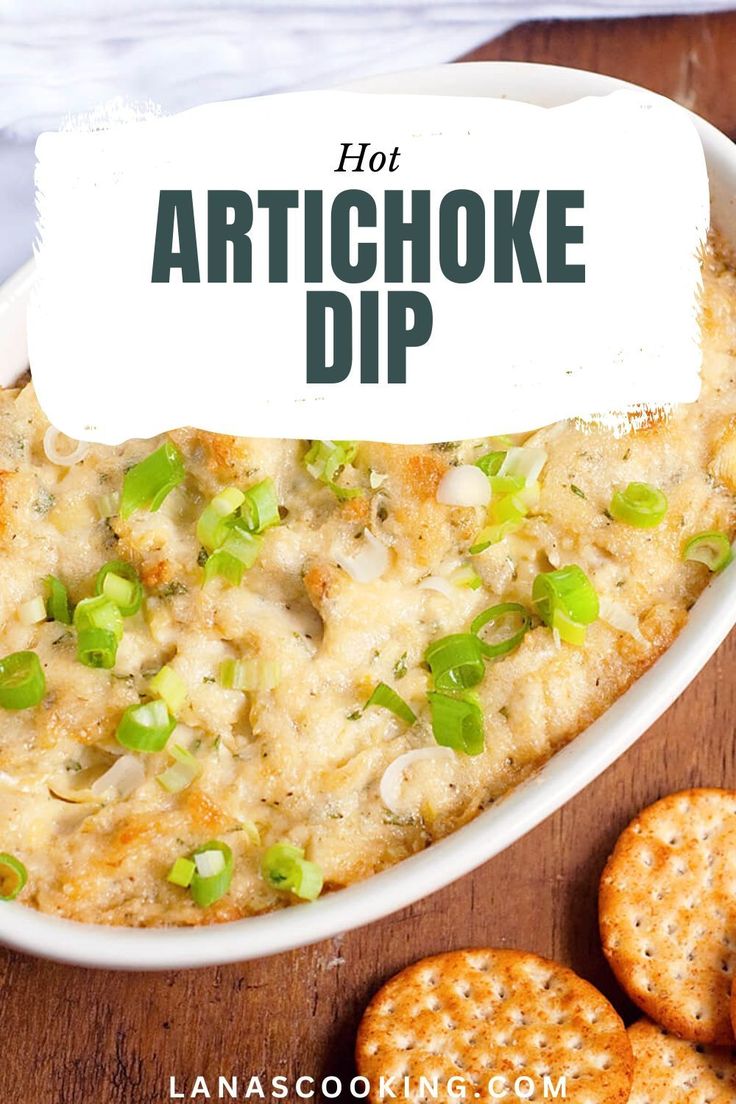 hot artichoke dip in a white bowl with crackers next to it on a wooden table