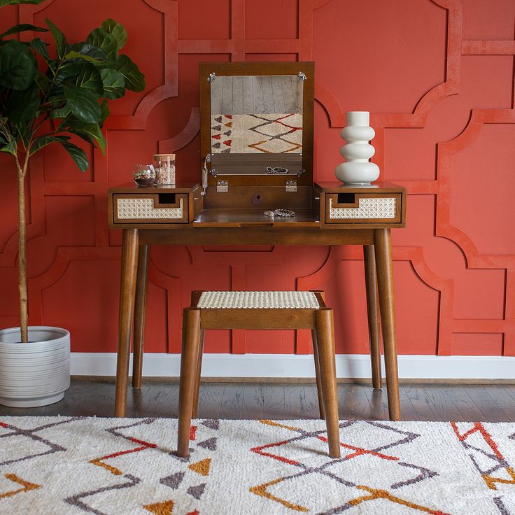 a desk with a mirror, stool and potted plant in front of an orange wall