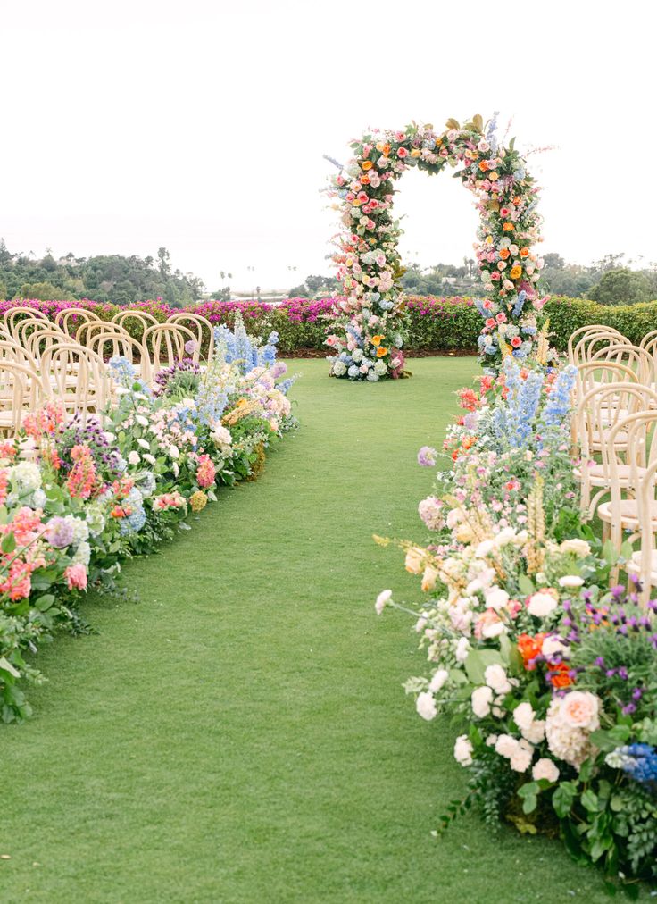 an outdoor ceremony with rows of chairs covered in flowers and greenery on the grass