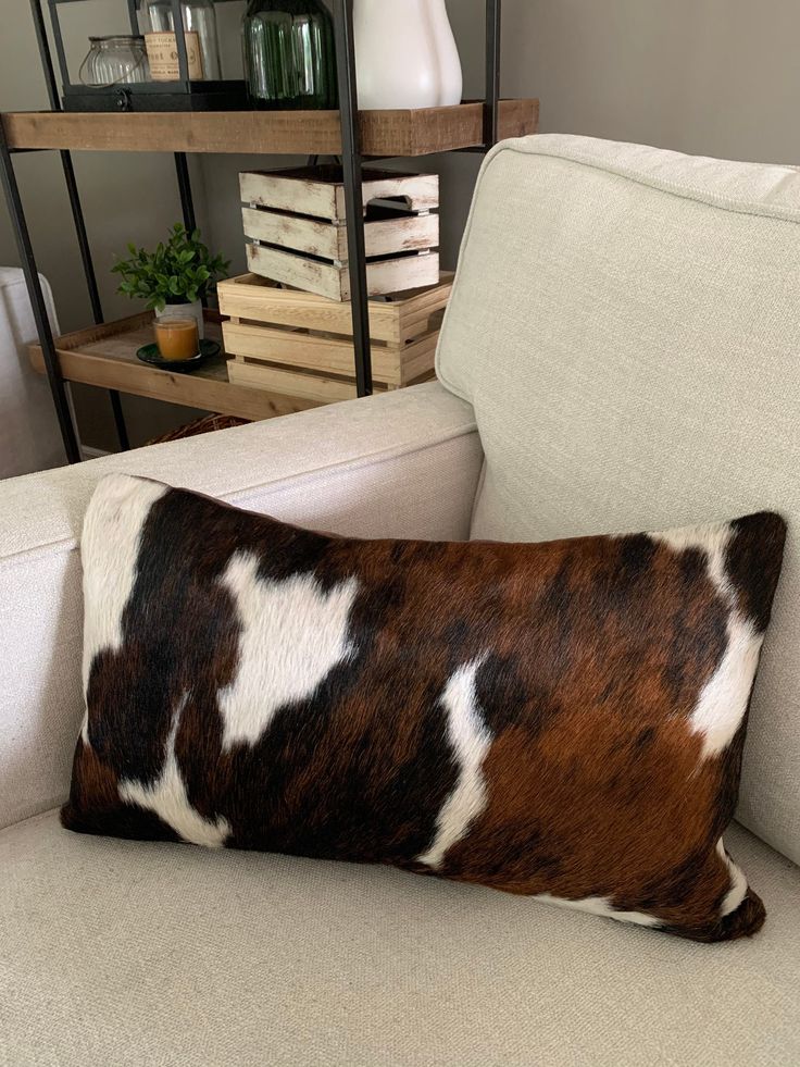 a brown and white cowhide pillow sitting on a couch next to a book shelf