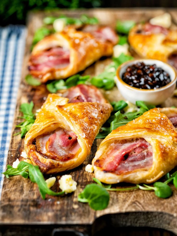 ham and cheese pastries on a wooden cutting board with garnishes in small bowls