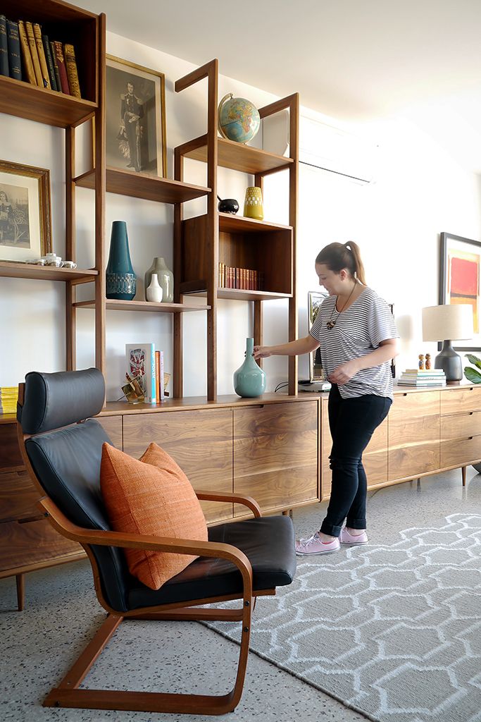 a woman standing in a living room next to a book shelf