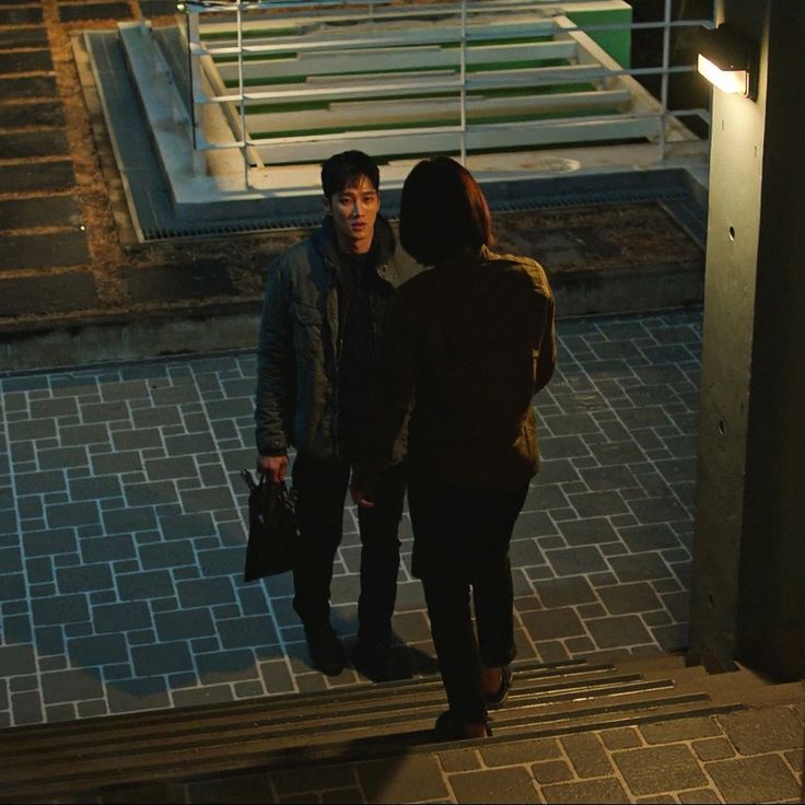 two people standing on the sidewalk at night talking to each other and one person holding a briefcase