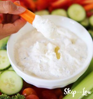 a person dipping dip into a bowl of celery, carrots and cucumbers