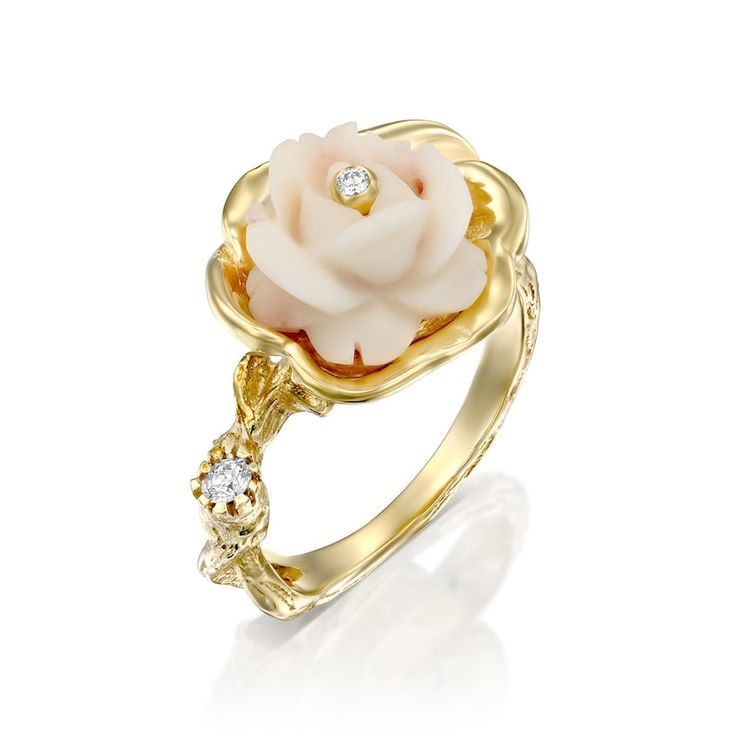 a gold ring with a white rose on the center and two diamonds in the middle