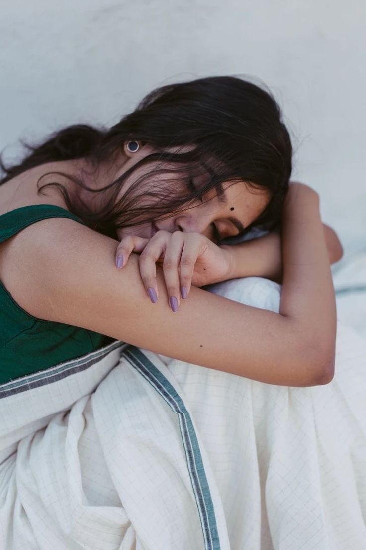 a woman laying on top of a bed next to a white wall and covering her face