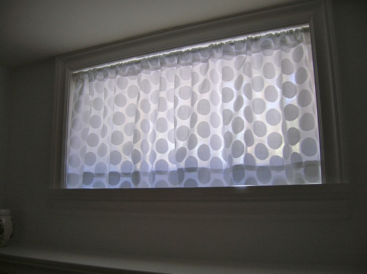 a window in a bathroom with white curtains and grey polka dots on the valance