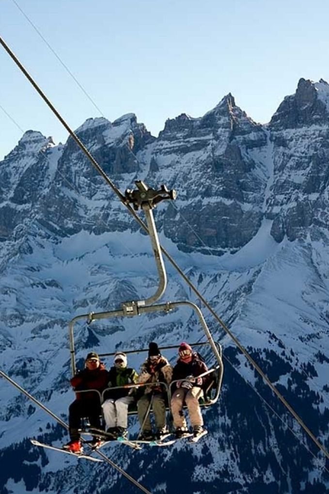 four people on a ski lift in front of snow covered mountain tops, with mountains in the background