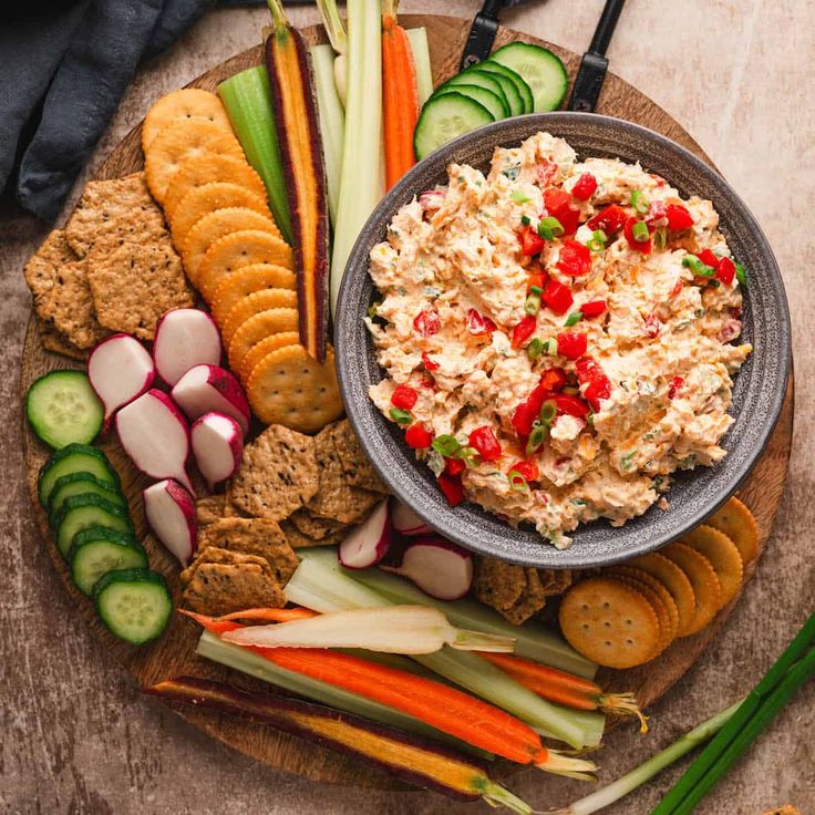 a platter filled with crackers, vegetables and dip