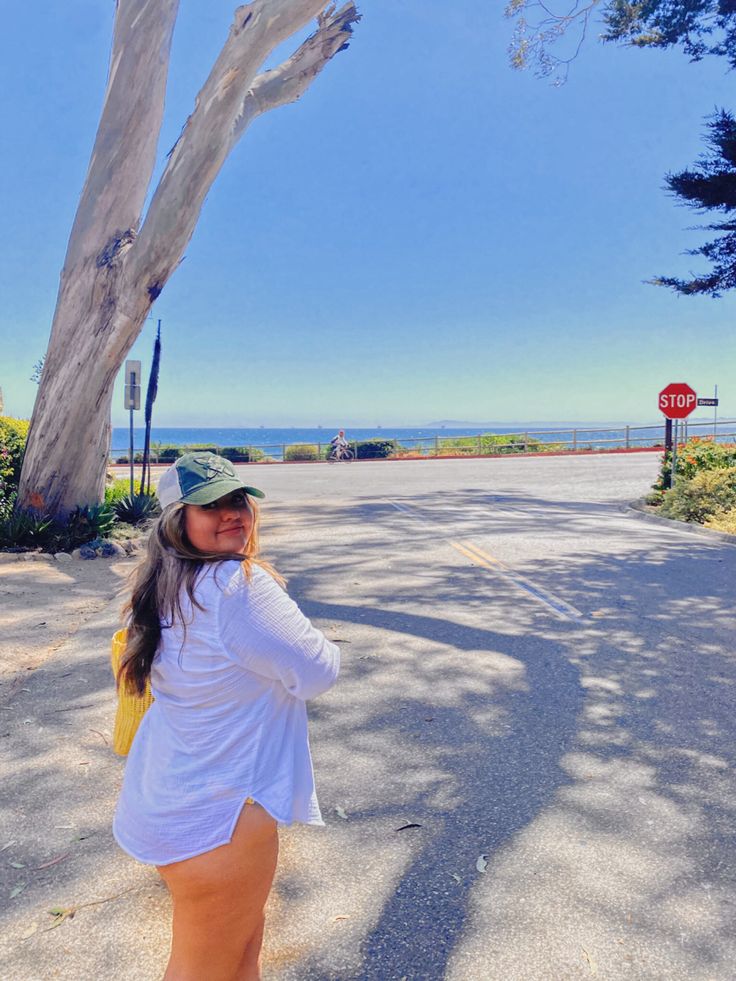 a woman standing on the side of a road next to a tree