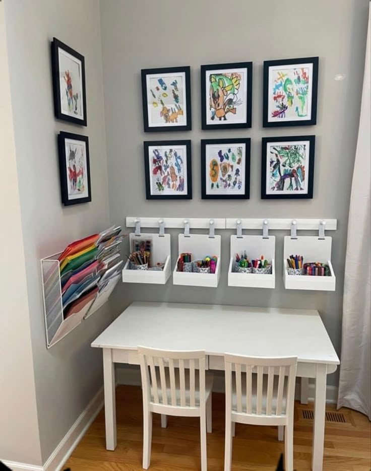 a white table and chairs in a room with pictures on the wall above it, along with small storage bins for children's artwork