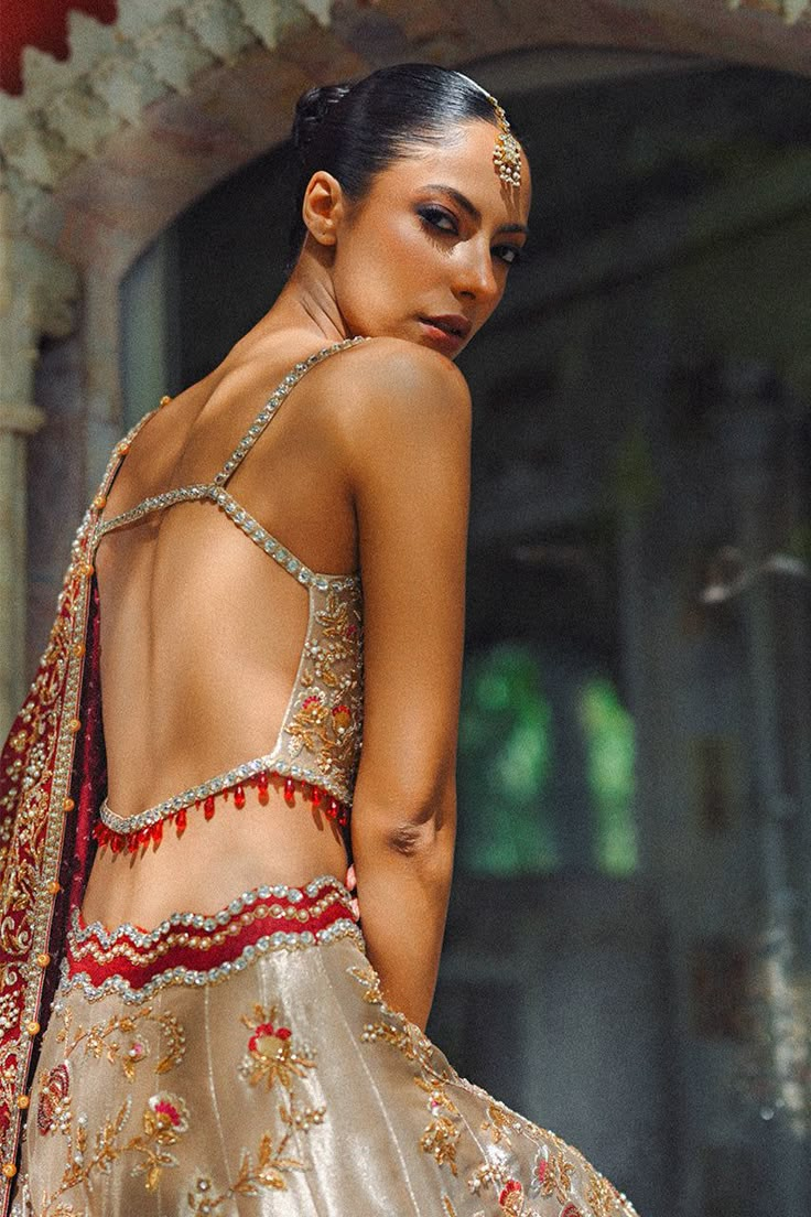 A gold tissue lehnga and choli features detailed zardoze and resham embroidery and is paired with a contrasting crimson cotton net dupatta adorned with gold zardoze borders and sequins. Gold And Red Lehenga, Gold Pre-draped Saree With Intricate Embroidery For Reception, Gold Pre-draped Saree With Sheer Dupatta For Eid, Traditional Tissue Silk Choli With Sheer Dupatta, Tissue Silk Choli With Sheer Dupatta, Traditional Choli With Sheer Dupatta In Tissue Silk, Gold Lehenga Saree With Mirror Work, Anarkali Style Gold Pre-draped Organza Saree, Reception Choli With Sheer Dupatta In Traditional Drape