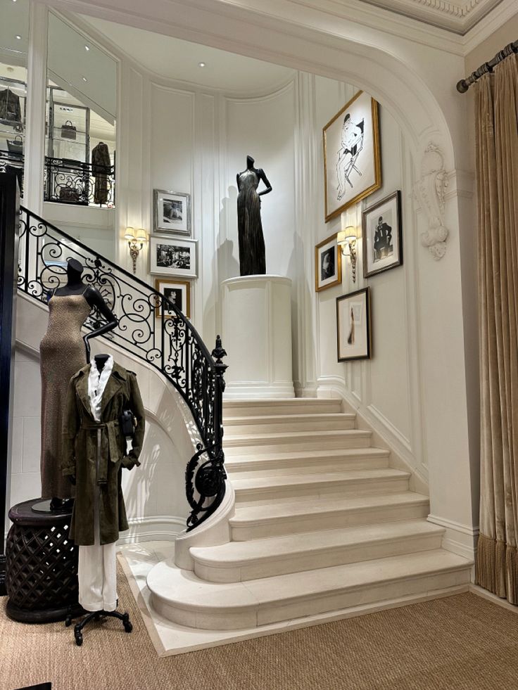 an elegant staircase with mannequins and pictures on the wall