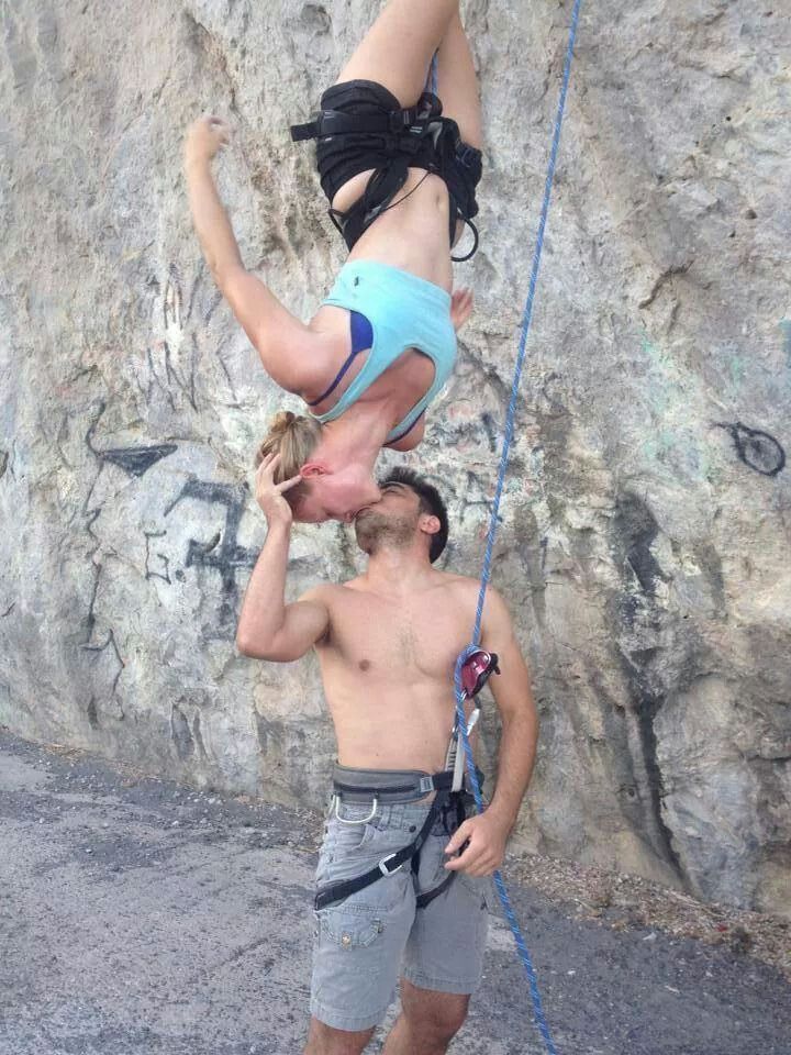 a man and woman climbing up the side of a rock face to face with each other