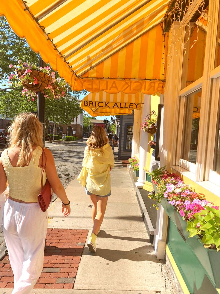 two women walking down the sidewalk in front of a building with yellow awnings