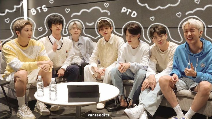 group of young men sitting on couches in front of a wall with clouds painted on it