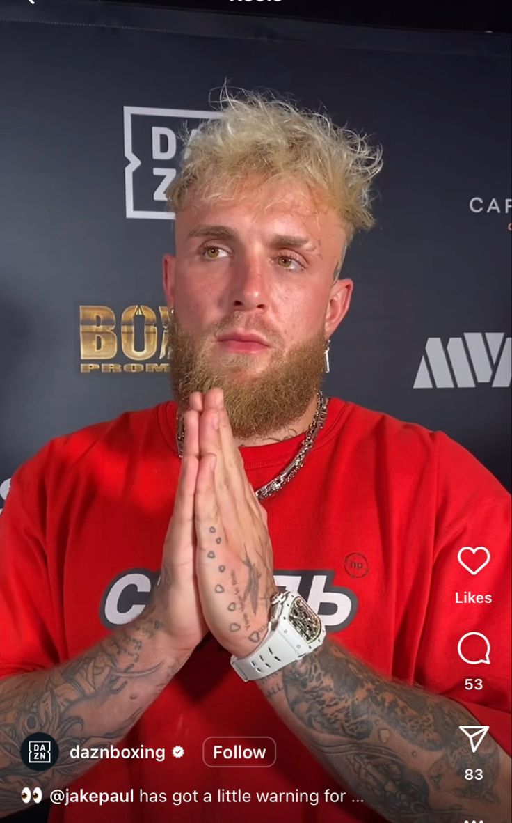 a man with blonde hair and beard wearing a red t - shirt is holding his hands together