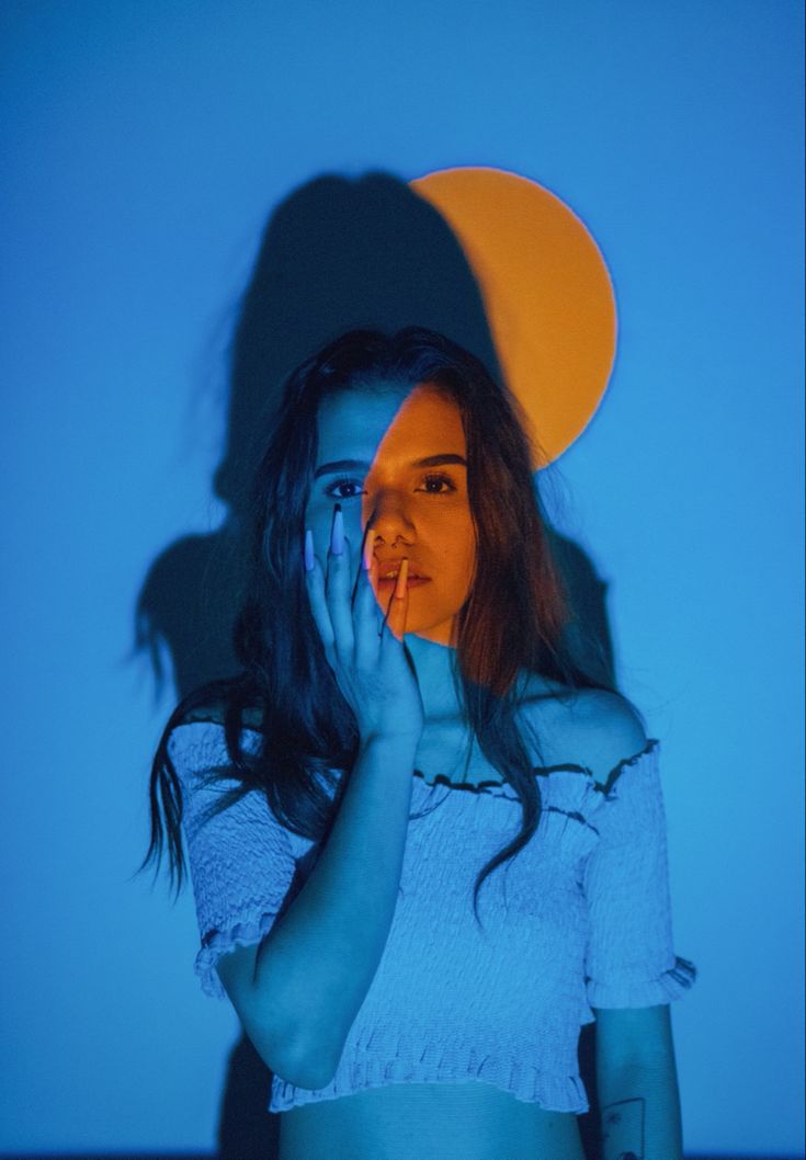 a woman wearing a hat and holding her hands up to her face in front of a blue background