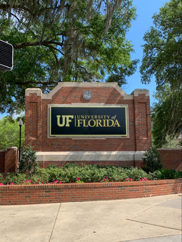 the university of florida sign is located in front of a brick building with trees and bushes around it