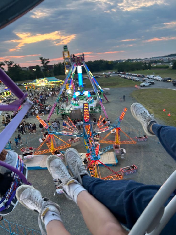 a person sitting on a ferris wheel at an amusement park with other rides in the background