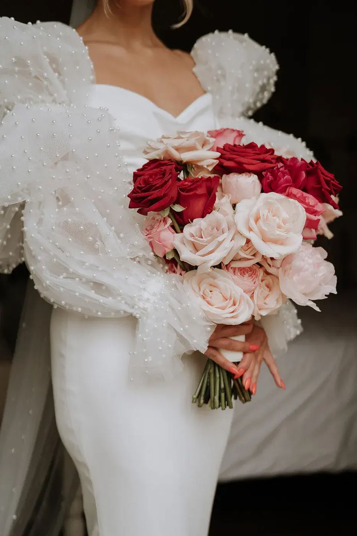 a woman holding a bouquet of flowers in her hand and wearing a white dress with ruffled sleeves