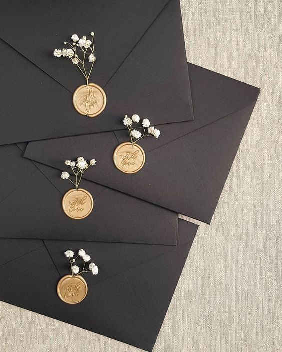 some black envelopes with gold buttons and flowers