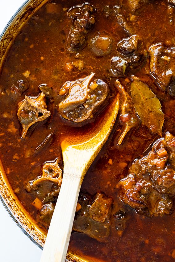 a wooden spoon in a pot filled with beef and mushroom stew on a white surface