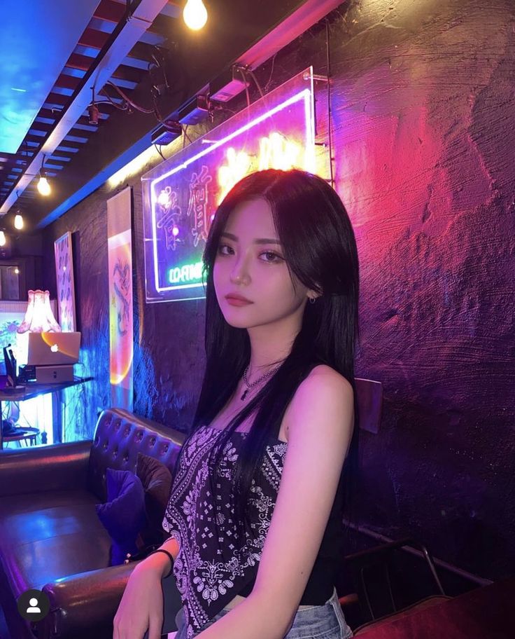 a woman standing in front of a bar with neon lights on the wall behind her