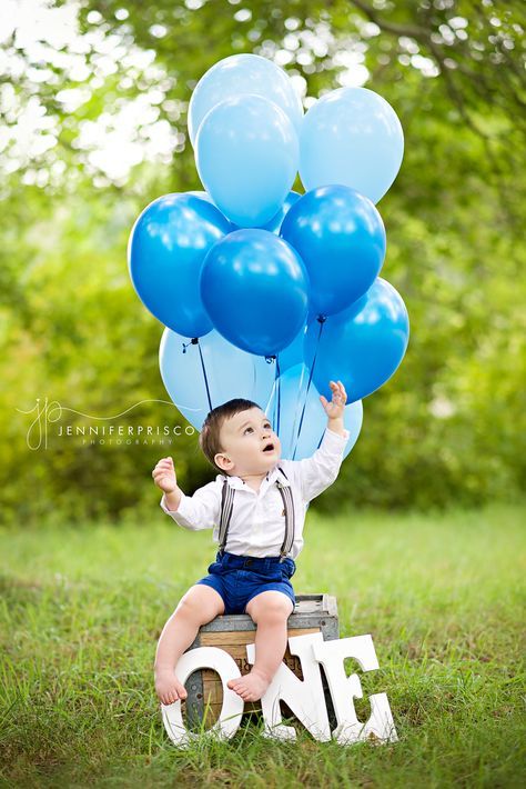 a little boy sitting on top of a wooden box holding blue balloons