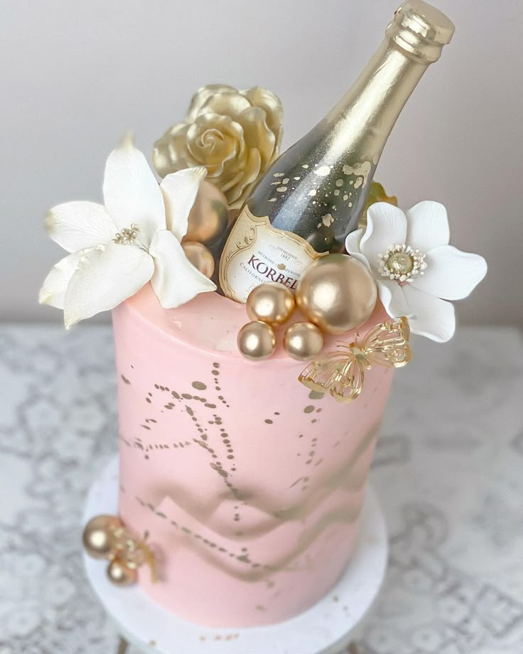 there is a pink cake with gold decorations on it and a bottle of champagne in the middle