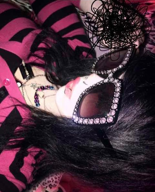 a woman with black hair and sunglasses laying on top of a pink bed covered in zebra print sheets